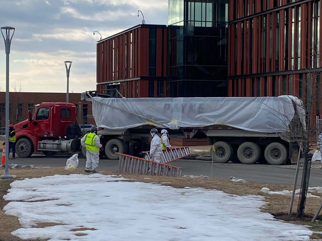 RETRO crew in protective suits loading regulated waste into a covered dump trailer outside a modern building