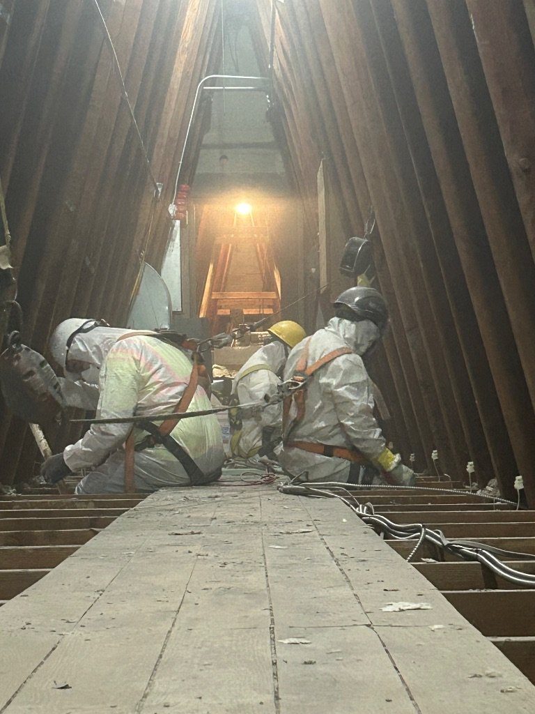 RETRO crew in protective suits, respirators, and fall-protection harnesses working on boards in an attic