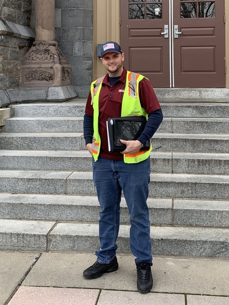 RETRO team member in a RETRO polo and safety vest, holding a project binder on the steps of a historic stone building