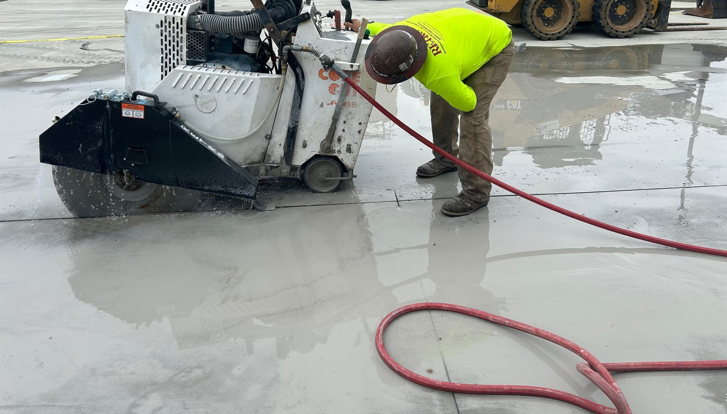 RETRO crew member running a walk-behind flat saw on a wet concrete slab, with water feeding the blade