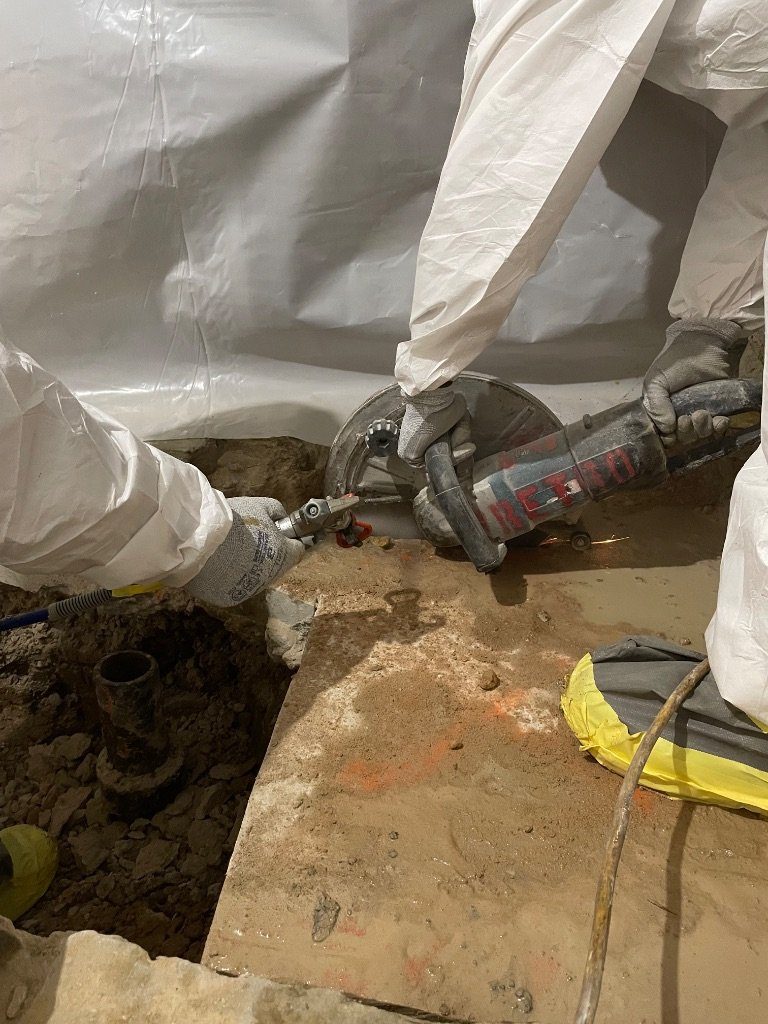 RETRO crew in protective suits wet-cutting a concrete slab with a RETRO cut-off saw inside poly containment