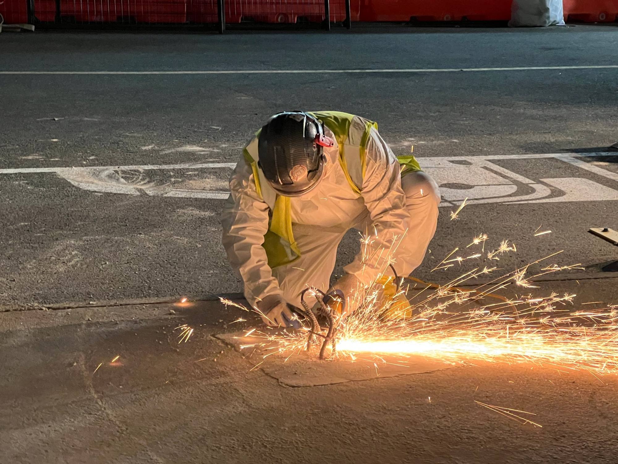 RETRO crew member in a protective suit and hard hat cutting rebar with a grinder, sparks flying