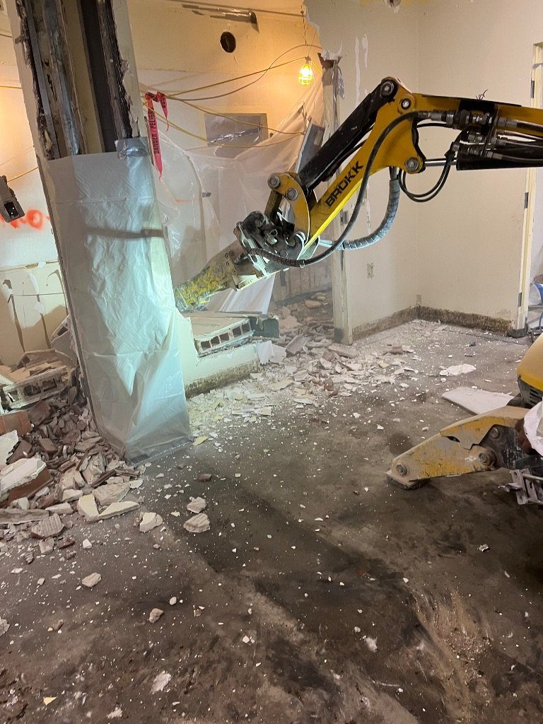 The BROKK® remote-controlled machine breaking out a wall next to a column wrapped in protective poly